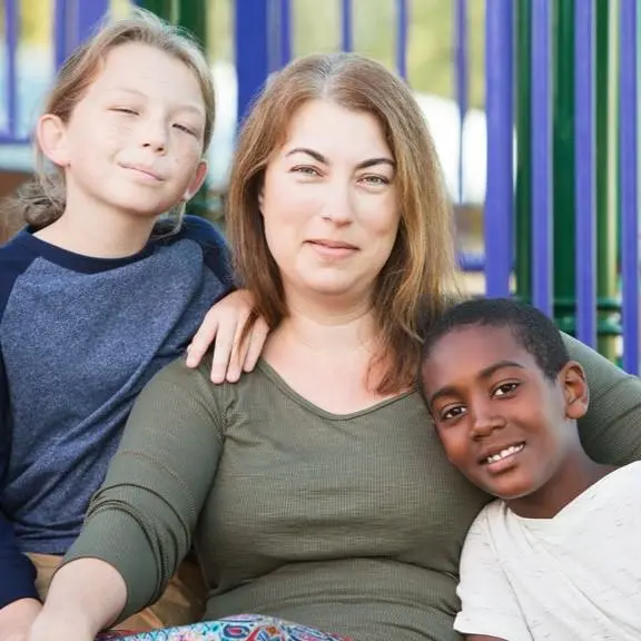 Foster mother sitting on playground playset with two foster children