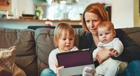 mum-with-toddler-and-baby-sitting-on-sofa-using-tablet
