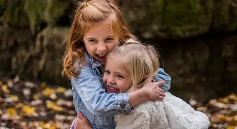 two-girls-hugging-autumn-leaves-on-the-ground