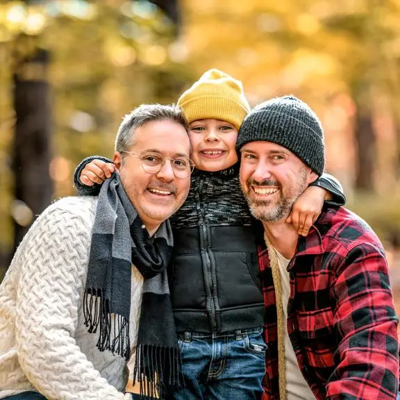 Two middle aged men crouching on either side next to a little boy in a forest in autumn